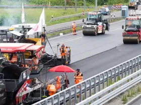 Arbeiter legen auf der ADAC A2 mit Maschinen und Walzen neuen Asphalt.